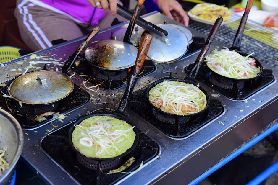 Street vendor cooking savory pancakes with veggies on a grill at an outdoor market.