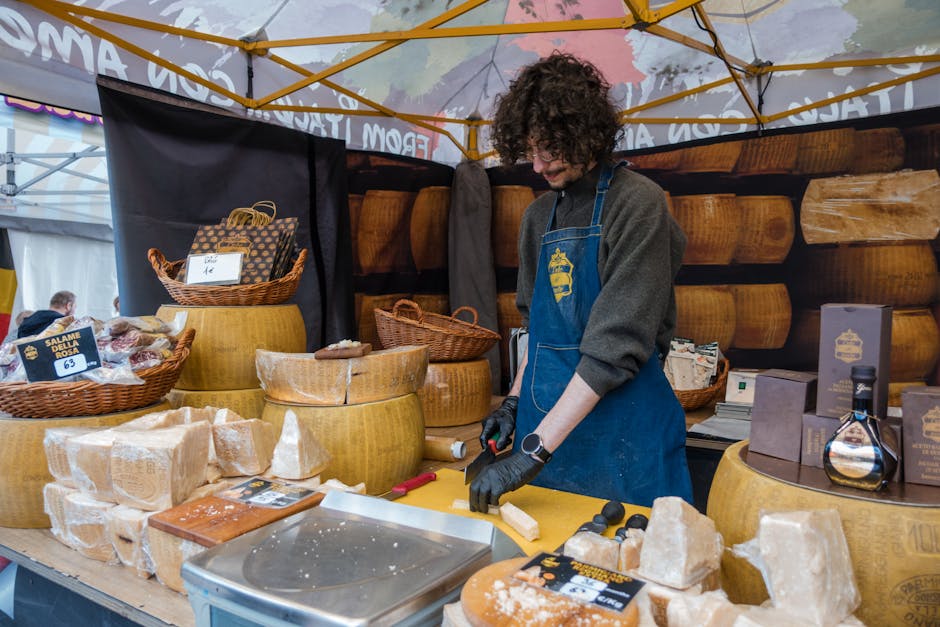 Young vendor slicing cheese at an outdoor market stall with various dairy products.
